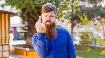 red hair bearded man feeling angry, annoyed, rebellious and aggressive, flipping the middle finger,...