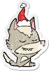 friendly distressed sticker cartoon of a wolf sitting wearing santa hat