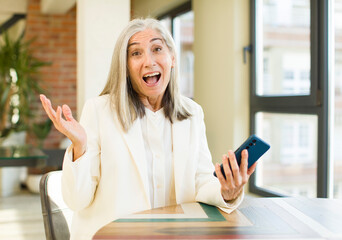 pretty senior woman feeling happy and astonished at something unbelievable with a smartphone