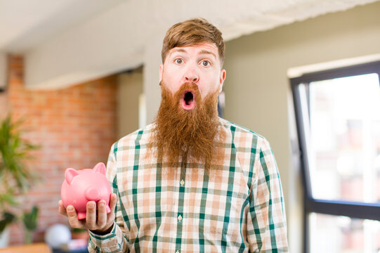 Red Hair Man Feeling Extremely Shocked And Surprised With A Piggy Bank