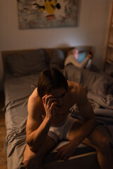 Obraz premium sad and shirtless man sitting on bed near blurred girlfriend, cheating concept.