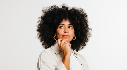 Thoughtful woman with curly hair standing against a studio background