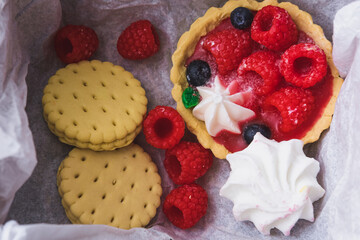 Tart, cookies, cake with whipped cream and raspberries packed in a box. Flat lay, top view.