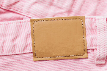 Pink jeans denim texture with thread sew lines. Fashion background with empty copy space for graphic design. Blank leather label tag. Brown clothing tag.