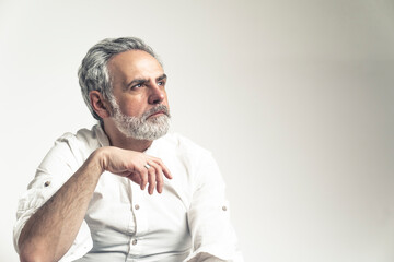 Gray haired bearded man wearing a white shirt looking away with a thoughtful expression. High quality photo