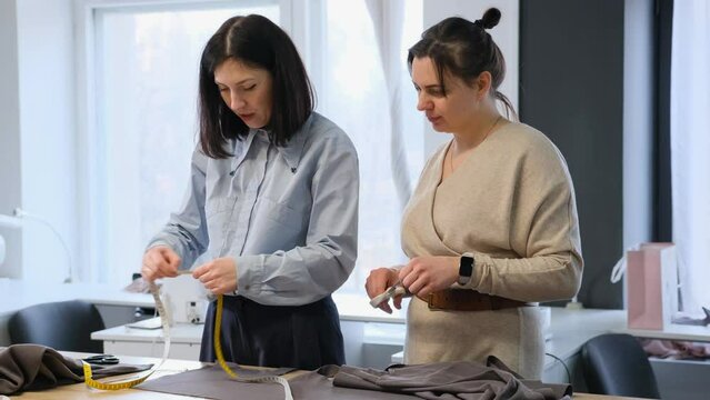 A Seamstress Girl Is Engaged In Teaching Sewing Production, Showing An Example To A Student How To Measure The Fabric Correctly