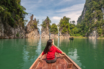 Boat riding through mountain lake view with woman tourist and tropical forest at Sam Klur mountain Khaosok National Park, Surat Thani Thailand nature landscape