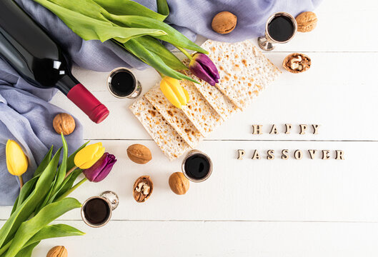 festive background with traditional treats for the jewish Passover holiday. White wooden background with happy passover letters and flowers.