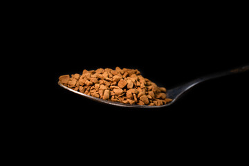 Close-up of instant granulated coffee in a teaspoon on a black background, macro photography