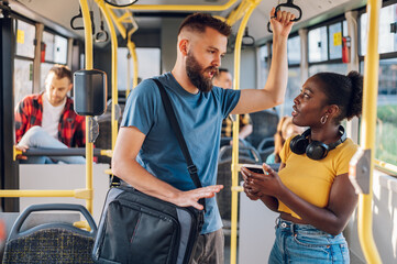 Multiracial friends talking and using a smartphone while riding a bus in the city