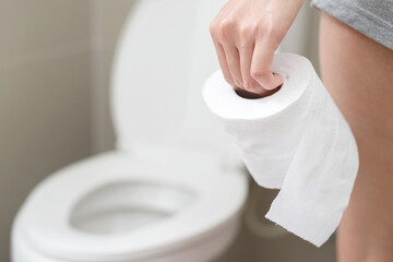 portrait of a woman suffers from diarrhea his stomach painful. ache and problem. hand hold tissue paper roll in front of toilet bowl. constipation in bathroom. Hygiene, health care concept.