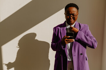 African american businesswoman using smartphone while standing over a white wall in an office