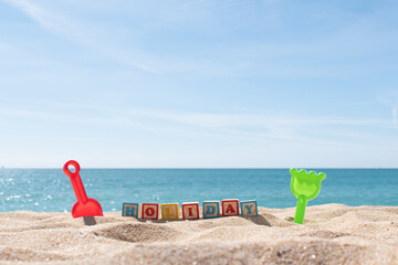 Holiday letters on cubes in the sand and ocean in the background. Copy space. Vacations background. Kids sand toys.