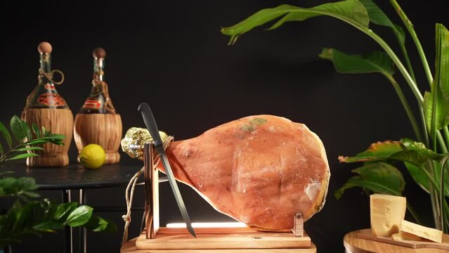 Fat jamon on wooden stand with knife, traditional cured ham served with parmigiano cheese, Italian or Spanish prosciutto leg ready for slicing