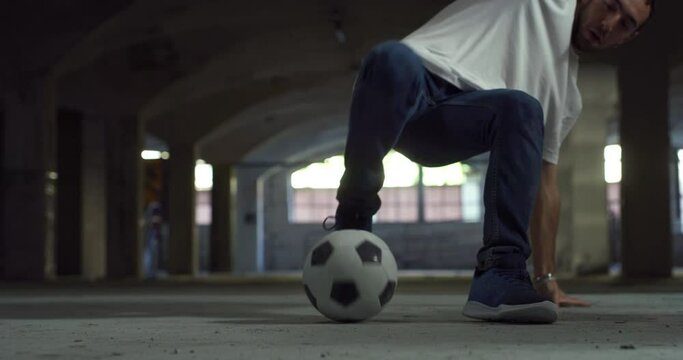 Low Angle, Ground Level Shot: Focus On The Legs Of A Talented Young Soccer Athlete Juggling A Ball Skilfully. Man Showing His Freestyle Football Skills In An Underground Parking Lot, Doing Tricks