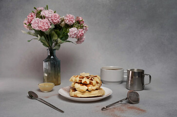 Homemade of tasty Waffles Plate, Caramel Sauce, Coffee Cup, Milk, pink flowers on a Grey Background