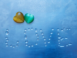 Two hearts and sign love made from water droplets on a blue metal surface.