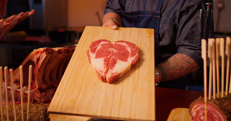 Cooks hands showing wooden board with raw beef ribeye steak meat. Juicy fresh meat steak on board...