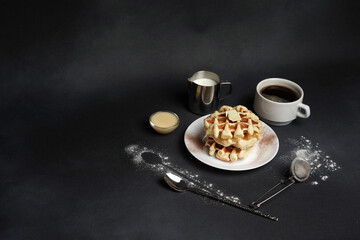 Homemade of Breakfast tasty Waffles, Caramel Sauce, Coffee Cup, Milk, dessertspoon, strainer on a Black concrete Background