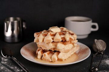 Homemade of tasty Belgian Waffles Plate, Caramel Sauce, Coffee Cup, Milk on a Black concrete Background