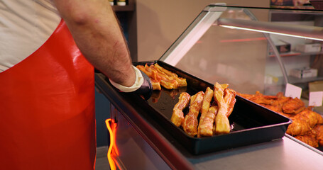 Butchers hands arranging meat on tray for display cabinet at shop. Male placing slices of meat in...