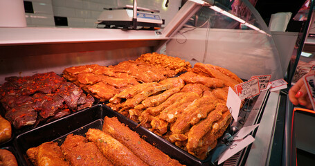 Marinated meat in window shop and woman hands changing the tag prices. Assorted seasoned pork and beef on display to be sold. Food industry.