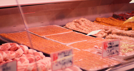 Minced meat in plastic containers in a window shop. Many packs of raw sausages from diverse animal meat for sale.