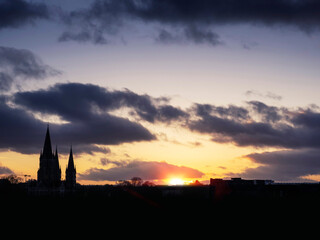 Silhouette of a spire of a catholic church against dark cloudy sunset sky and setting sun