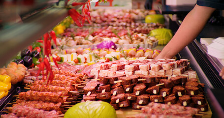 Man hands in gloves placing a tray full of pieces of meat on skewers. Butchery worker fulfilling the gaps with pregessed meat.