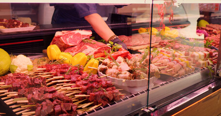 Mens hands picking chicken barbecue on skewers to be weighted. Window shop with different meat goods in butchers store.