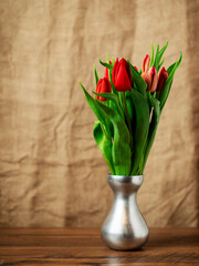 Beautiful bouquet of red tulips. Brown color hessian cloth in the background. Selective focus. Still life. Gift to woman on a special occasion.