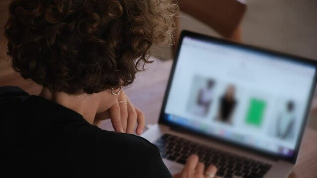 Young caucasian woman with her back to the camera works on a personal computer. A woman designer browses websites and stores with clothes, analyzes fashion trends in the fashion industry.