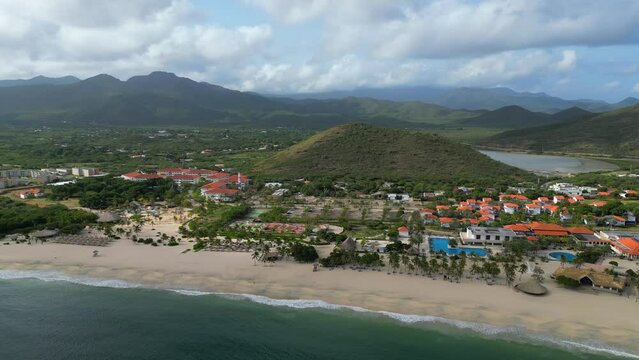 Aerial panoramic view of the Puerto Cruz beach on the Margarita island at dawn. Sandy coast with all inclusive resorts and lighthouse on the cliff. Vacation in Venezuela 