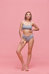 Fototapeta na wymiar Portrait of young thin sportive woman in grey cotton inner wear posing over pink background. Concept of natural beauty, body and skin care, healthy eating
