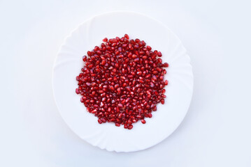 Pomegranate seeds, or kernels on the plate. Juicy pomegranate arils showing beautiful shades of red against white background, top view. Bright colors of ripe tasty fruit, healthy food concept.