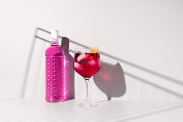 Refrescante gin tónica rosa adornado con naranja sobre un fondo con sombras
