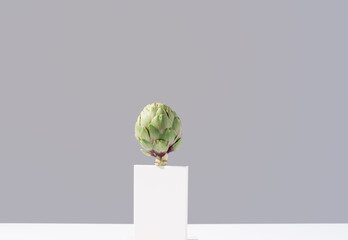 Flor de alcachofa cruda en pie sobre una mesa blanca y fondo gris