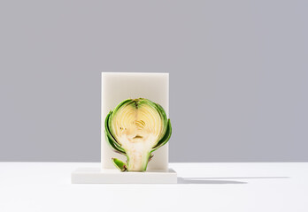 Alcachofa partida por la mitad sobre un soporte blanco y fondo gris	