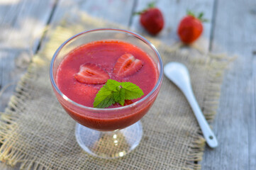 Strawberry smoothie in a glass decorated with mint leaves on rustic background, fresh fruit juice is red, detox food, diet and healthy breakfast, top view