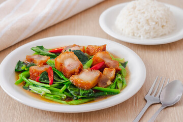 Stir fried kale with crispy pork in oyster sauce and rice on white plate