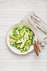 Healthy green avocado salad bowl with boiled eggs, sliced cucumbers, edamame beans, olive oil and herbs on ceramic plate top view on white wooden rustic table background