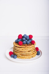 Delicious freshly cooked thick and fluffy protein pancakes served on white plate whith fresh fruit. Healthy food, low carb diet. Negative space for text.