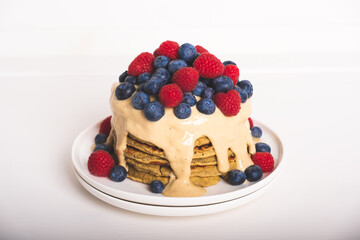Delicious freshly cooked thick and fluffy protein gluten free pancakes stacked on white plate, served with cashew cream and fresh berries. Healthy food