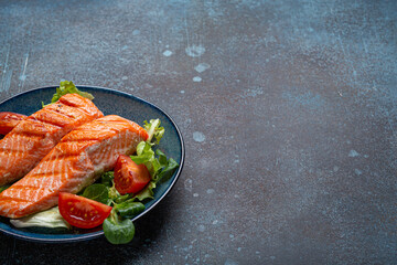 Grilled fish salmon steak with vegetables salad on ceramic plate on rustic stone background angle view, balanced diet or healthy nutrition salad meal with salmon and veggies, space for text