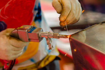 Welder hands using portable handheld laser welding machine with sparks - close up. Manufacturing,...
