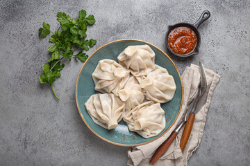 Georgian dumplings Khinkali on plate with red tomato sauce and fresh cilantro top view on rustic stone background, traditional dish of Georgia