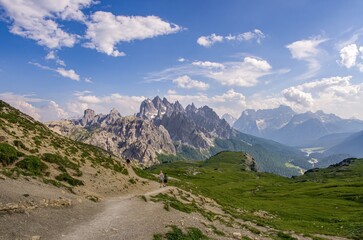 beautiful mountain landscape with sharp edges, green meadows and tourists on the trail. Italian Dolomites, tourist topic and sport.
