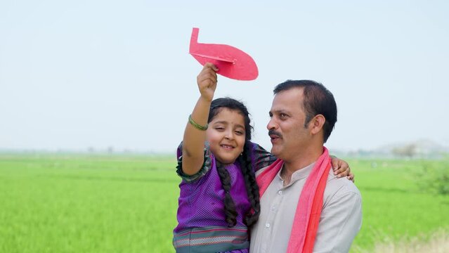 Happy village girl kid playing with airplane toy while father holding or carrying near farmland - concept of relationship, parental caring and healthy lifestyle
