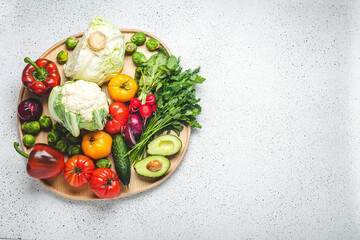 Rustic wooden tray with selection of fresh vegetables and greenery on white kitchen table top view. Vegetarian or diet food from organic ingredients, healthy nutrition concept, space for text