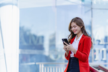 Outdoor portrait of elegant smiling woman in red dress holding smartphone. Cheerful woman using...